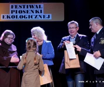 prezes spółki komunalnej, zastępca burmistrza i franciszanin na scenie wręczają nagrody